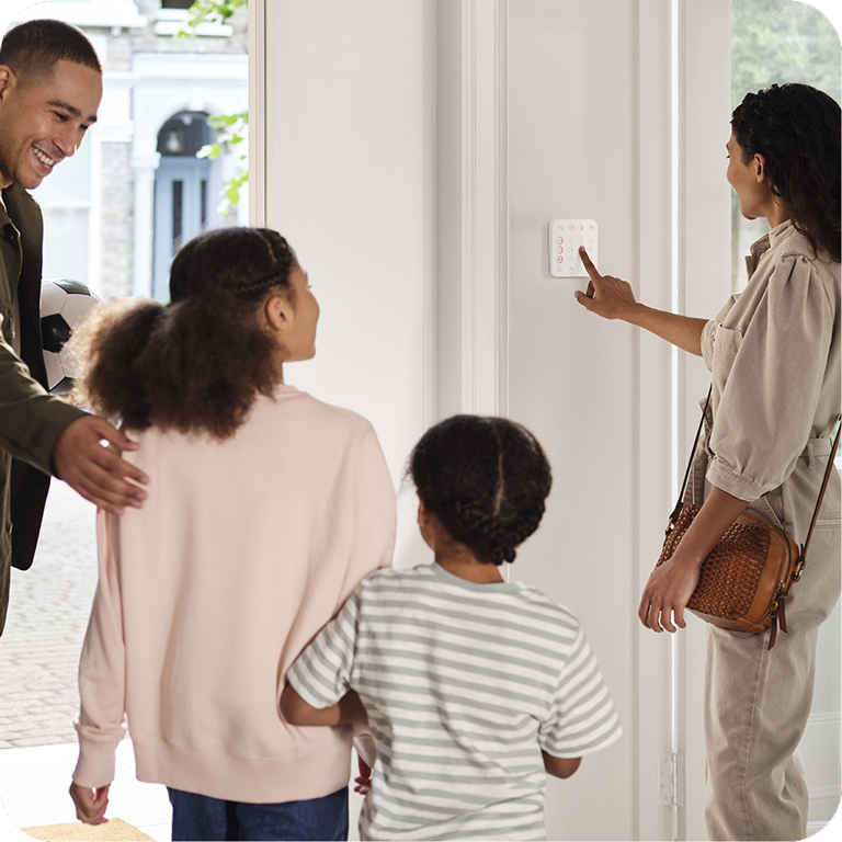 A family is standing in front of a RIng security panel whilst mum presses the buttons